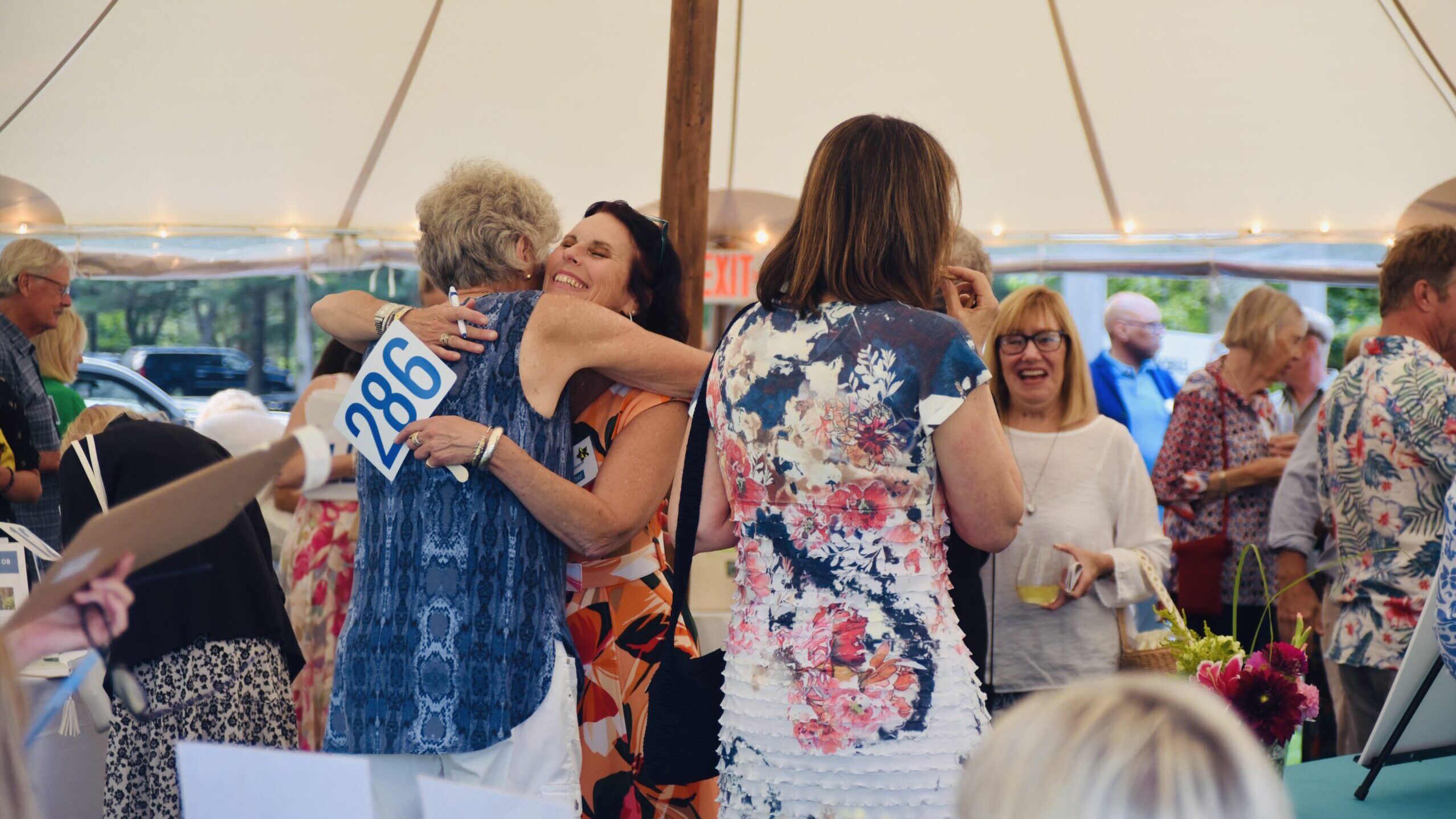 Friends share a hug under the silent auction tent at the Summer Soiree