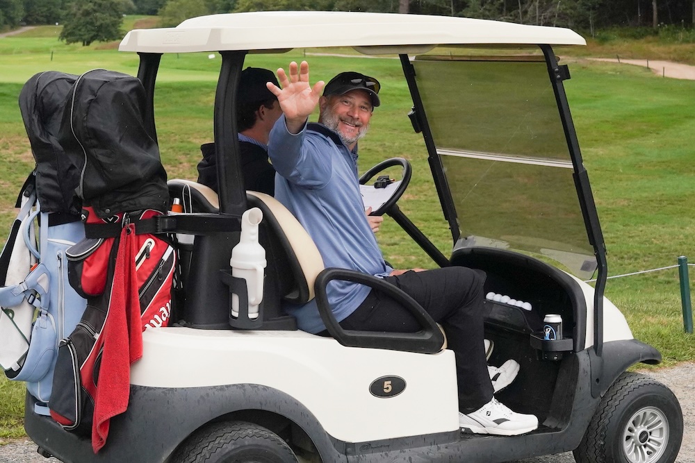 Plauer waving from the passenger seat of a golf cart