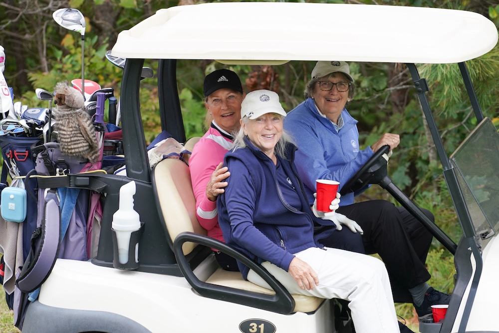 Smiling ladies team driving a golf cart 